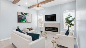 Un salon moderne avec des canapés blancs, une cheminée, un téléviseur fixé au mur et un ventilateur de plafond.