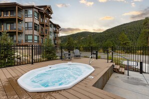 Une terrasse en bois avec un jacuzzi, un espace clôturé et une vue sur une montagne et une forêt.