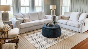 Un salon moderne avec deux canapés blancs, un pouf bleu et un tapis à carreaux.