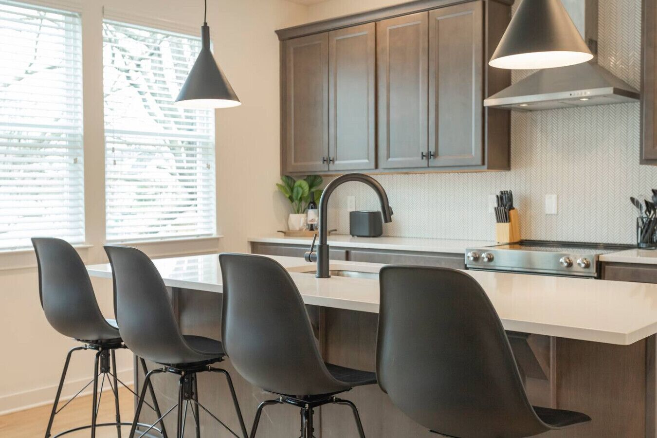 A modern kitchen with a central island, bar stools, pendant lighting, and a view of the outdoors.