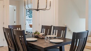 Een eetkamer met een donker houten tafel voor zes personen, omringd door zes stoelen. Daarboven hangt een moderne kroonluchter.