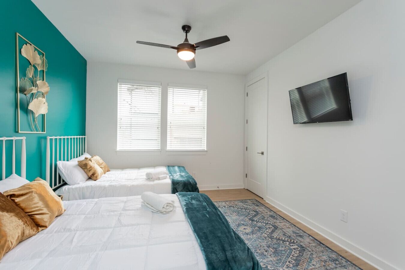 A bedroom with two beds, a ceiling fan, a TV, and a window with blinds.