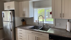 A modern kitchen with white cabinets, stainless steel appliances, and a window with a view of greenery.