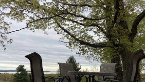 An outdoor seating area with a table and chairs, surrounded by trees and a view of the landscape.