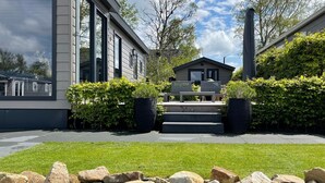 A modern building with a central entrance, large windows, and a well-maintained lawn with rocks in the foreground. - PUUR Eernewoude luxury cabin on open water in the Alde Feanen (Earnewald)