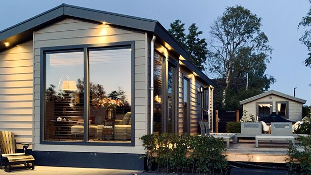 A modern house with large windows, a deck, and outdoor seating. - PUUR Eernewoude luxury cabin on open water in the Alde Feanen (Earnewald)