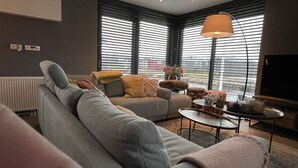 A modern living room with a grey sofa, a coffee table, and a TV. - PUUR Eernewoude luxury cabin on open water in the Alde Feanen (Earnewald)