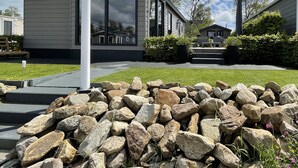 A modern house with a large window, a stone pathway, and a well-maintained lawn. - PUUR Eernewoude luxury cabin on open water in the Alde Feanen (Earnewald)