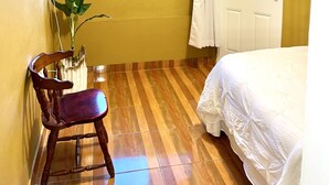 Une pièce comprenant un lit, une chaise, une fenêtre donnant sur des palmiers, un ventilateur et une porte.