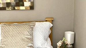 A neatly made bed with a patterned pillow and a white pillow, a bedside table with a vase of flowers, and a wall-mounted artwork. - Well equipped dog friendly cottage ideal for relaxing, walking, cycling, golf (Crieff)