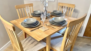 A wooden dining table set with grey plates, cutlery, and wine glasses, surrounded by wooden chairs with cushioned seats. - Well equipped dog friendly cottage ideal for relaxing, walking, cycling, golf (Crieff)