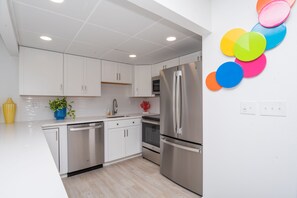 A modern kitchen with white cabinets, stainless steel appliances, and a colorful wall decoration.