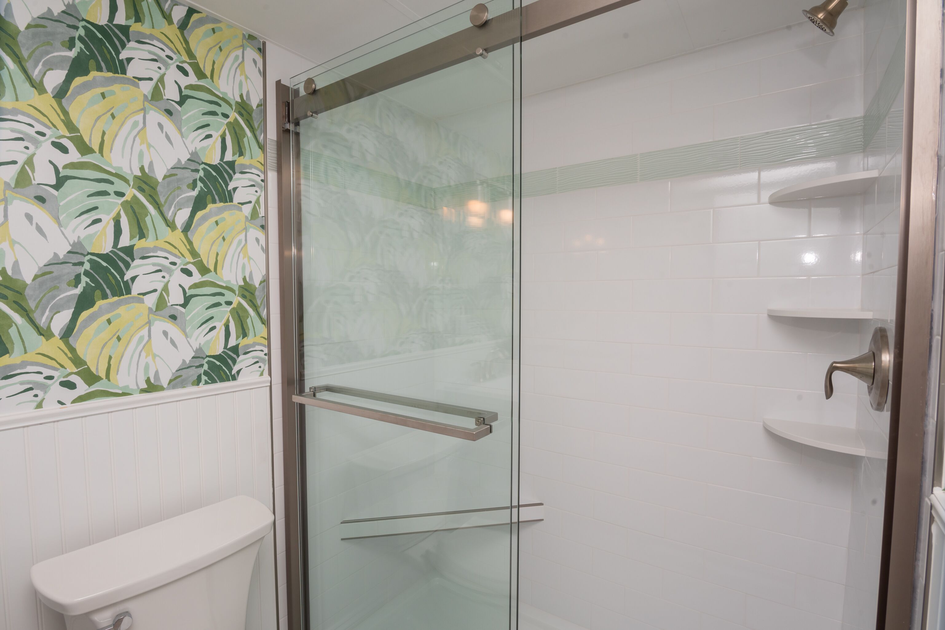 A bathroom with a glass shower enclosure, white tiles, and a toilet.