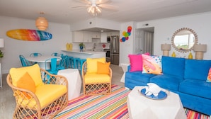 A bright living room with a blue sofa, yellow and blue chairs, a colorful striped rug, and a kitchen in the background. - Beautiful Ocean views, Just renovated 2 bedroom 2 bath Condo, 2 parking spots  (Ocean City)