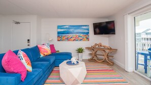 A living room with a blue sofa, colorful pillows, a wooden coffee table, a striped rug, a painting, and a TV on the wall. - Beautiful Ocean views, Just renovated 2 bedroom 2 bath Condo, 2 parking spots  (Ocean City)