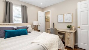 Ein Schlafzimmer mit Bett, Schreibtisch, Stuhl und zwei gerahmten Kunstwerken an der Wand.