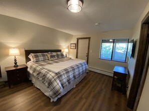 Ein Schlafzimmer mit Bett, Nachttischen, einem Fenster und einer Tür.