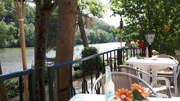 A riverside terrace with a table and chairs, surrounded by trees and a view of the water. - Harzglück Albertine 505 (Güntersberge)