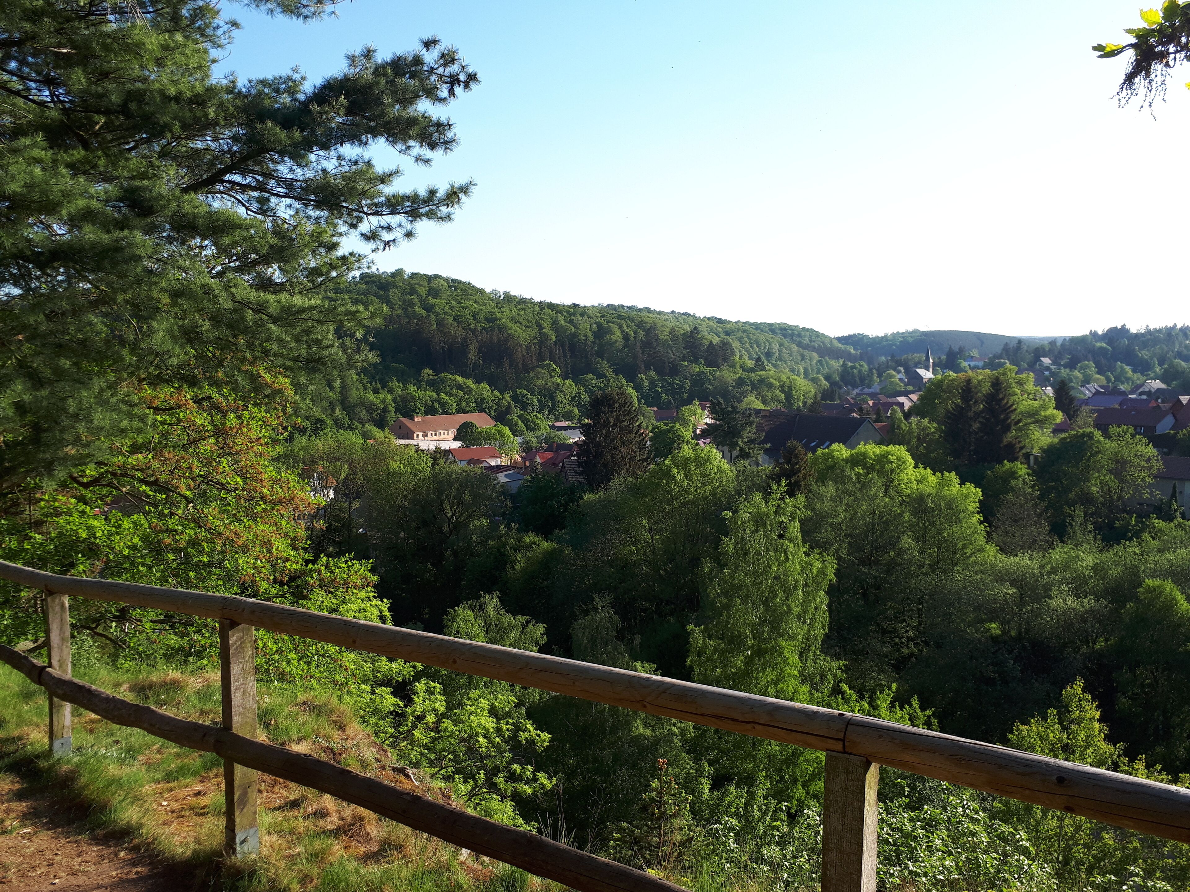 Una vista panorámica de un pueblo situado en un valle boscoso, con una valla de madera en primer plano.