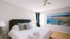 A bedroom with a large bed, a nightstand, a lamp, and a painting of a beach scene.