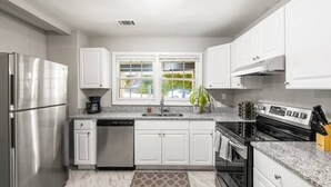 Une cuisine moderne avec des meubles blancs, des appareils en acier inoxydable, un plan de travail en granit et une fenêtre donnant sur un espace verdoyant.