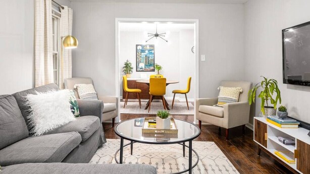 Un salon moderne avec un canapé gris, une table basse et un coin repas avec des chaises jaunes.