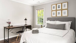 Une chambre à coucher avec un lit, un bureau et une chaise. Il y a une fenêtre qui donne sur un paysage verdoyant.