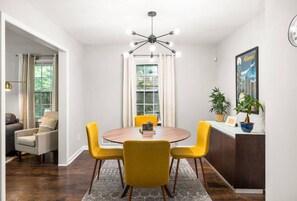 Un espace repas avec une table ronde, des chaises jaunes, un lustre moderne et une vue sur l’extérieur grâce à de grandes fenêtres.