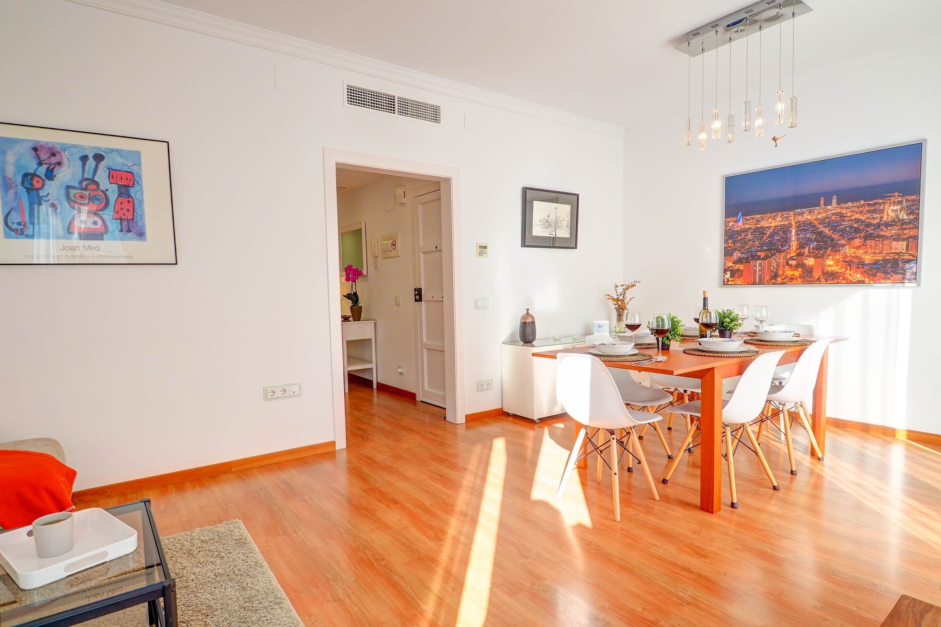 A modern dining area with a wooden table and white chairs, a cityscape view, and a framed artwork on the wall.