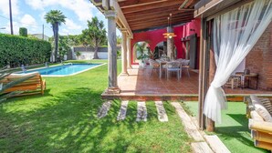 A covered patio area with a pool, outdoor seating, and a red wall. - Villa Nirvana by Hello Homes Sitges (Sitges)