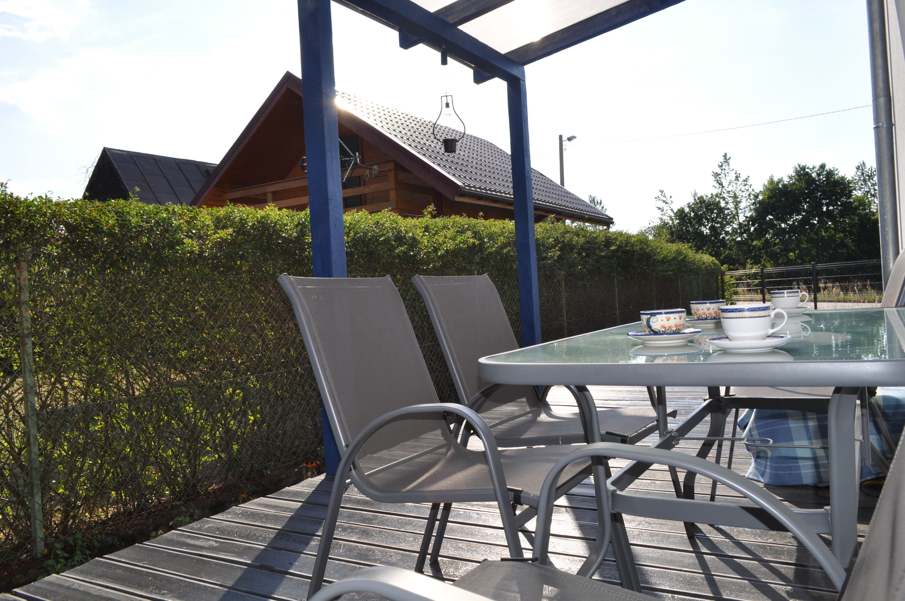 Une table en verre, des chaises en métal et une tasse blanche posée sur une terrasse en bois.