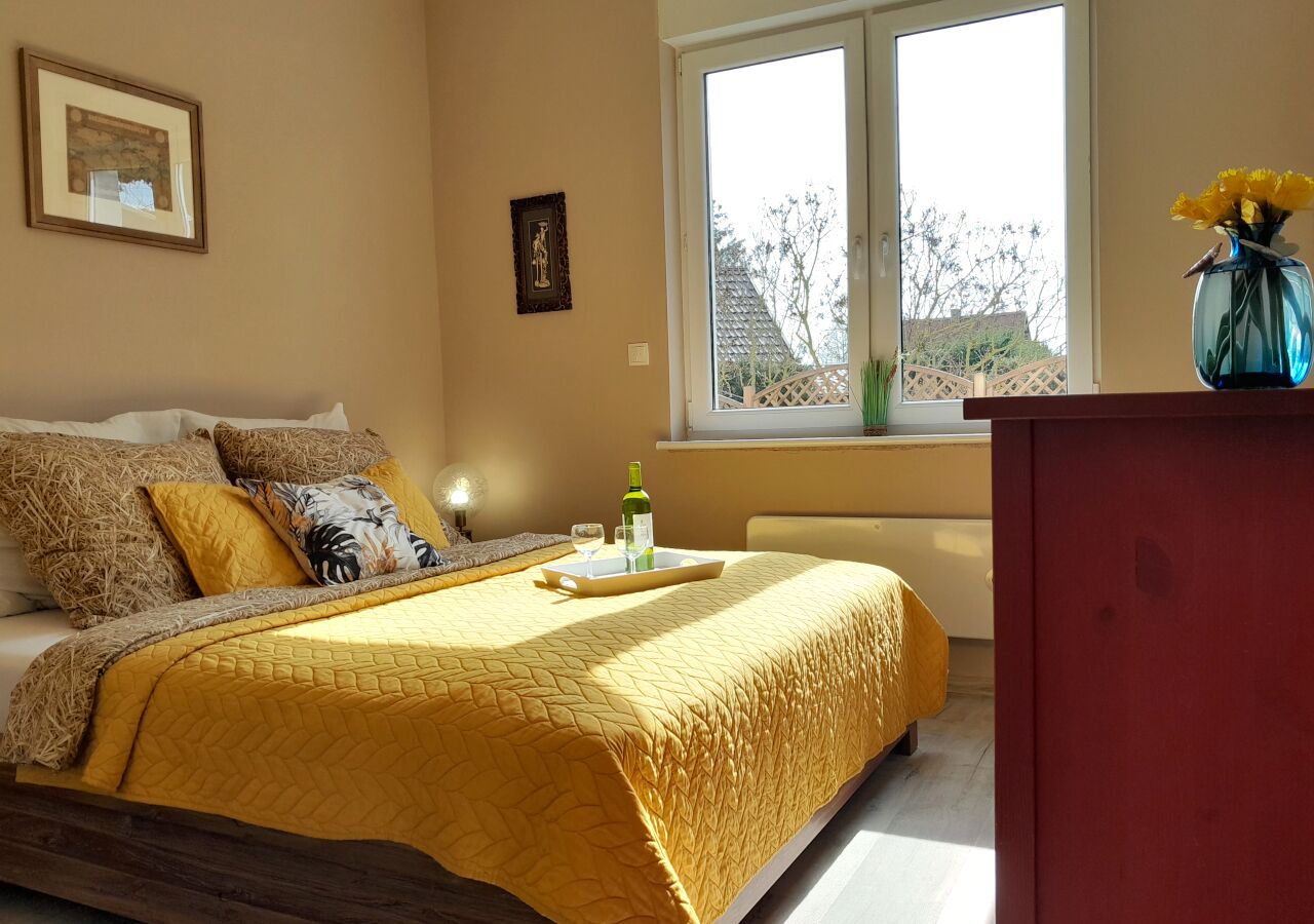 A bedroom with a bed, a nightstand, a window, and a vase with flowers on the windowsill.