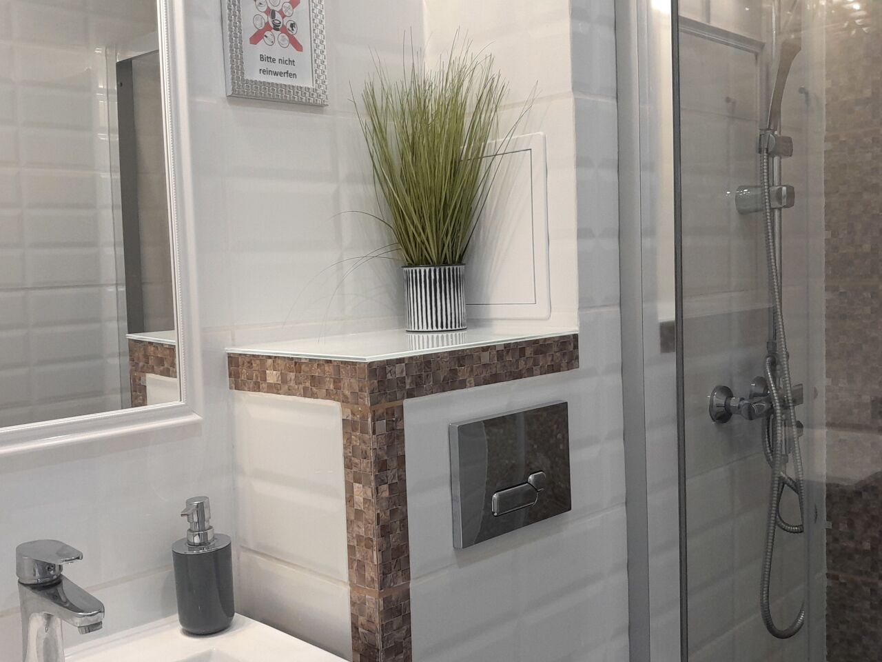 A bathroom with a glass shower enclosure, a sink with a modern faucet, and a potted plant on the vanity.