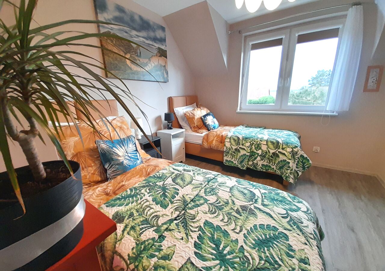 Une chambre avec deux lits, une table de chevet, une lampe, une plante en pot et une fenêtre avec des rideaux.