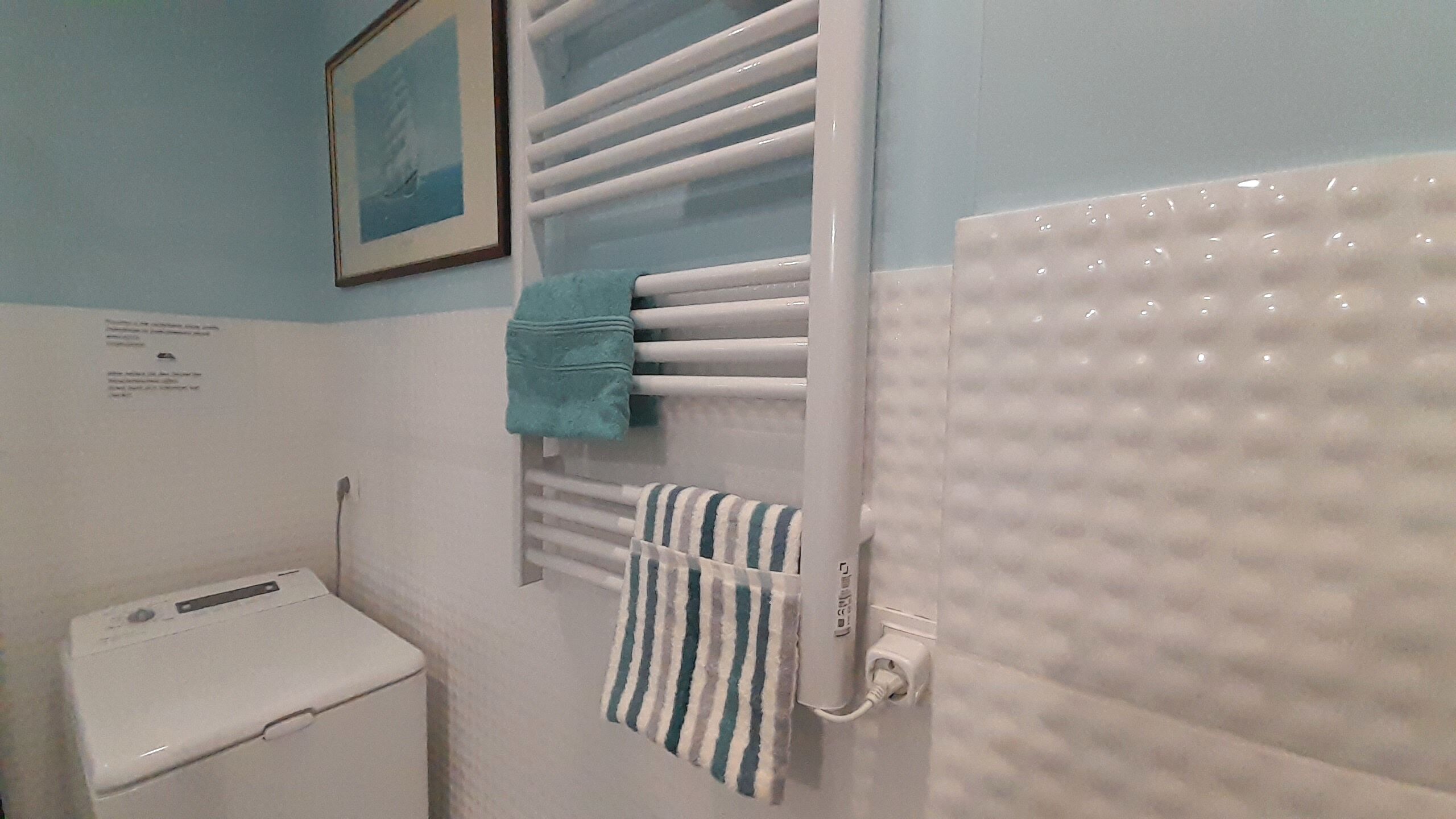 Een badkamer met een witte badkuip, een wit toilet, een handdoekrek met twee handdoeken en een lijst met een afbeelding aan de muur.