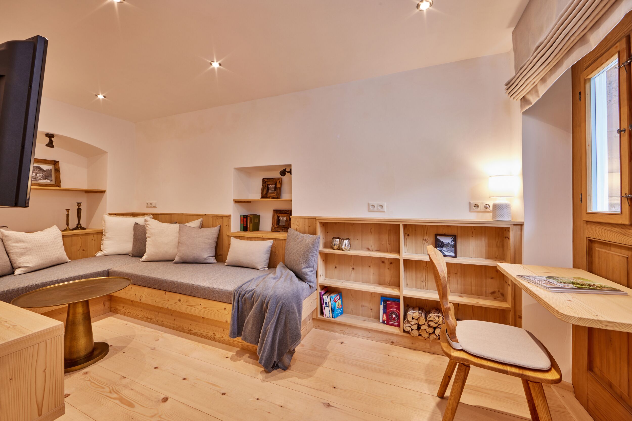 A cozy room with a wooden floor, a sofa, a wooden chair, a small table, and shelves with books and decorative items.