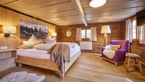 Un dormitorio de cabaña de madera con una cama, un sillón morado, un taburete pequeño y un cuadro en la pared.