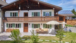 Una cabaña de dos pisos con balcón, fachada de madera y zona de comedor con mobiliario exterior.