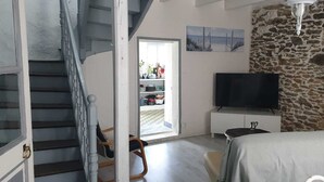 Un dormitorio con pared de piedra, televisión, cama y una escalera que lleva a un balcón.
