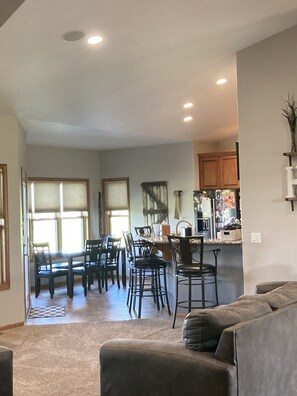 Ein geräumiges Wohnzimmer mit einer großen grauen Couch, einem Essbereich mit einem Holztisch und Stühlen sowie einer Küche mit Holzschränken und einem Kühlschrank.