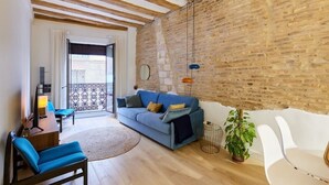 Un salon moderne avec un canapé bleu, des poutres en bois, un mur en briques et un balcon doté d’une balustrade à motifs.