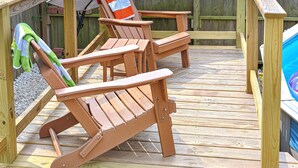 Eine Holzterrasse mit zwei Adirondack-Stühlen und einem Pool.