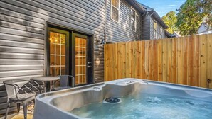 A hot tub in a backyard with a wooden fence, a door, and a small table with chairs.
