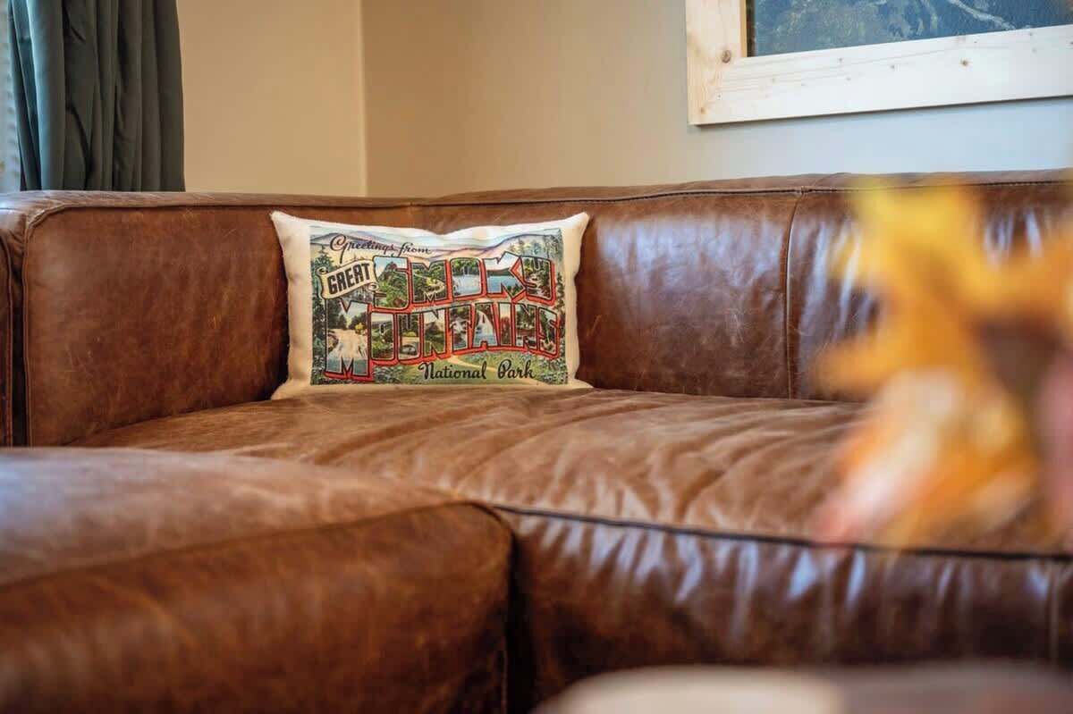 A brown leather sofa with a cushion featuring a vintage-style design.