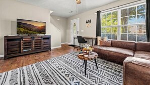 A living room with a TV, a brown leather sofa, a patterned rug, and a ceiling fan.