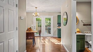 A hallway with a dining area, a chandelier, and a view of the outdoors through glass doors.