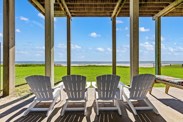 Una terraza de madera con tres sillas Adirondack mirando hacia la playa.