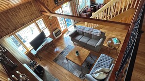 A spacious loft-style room with a high ceiling, wooden beams, a large sofa, a coffee table, and a television.