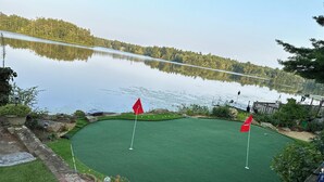 A golf course with two flags, a pond, and a forest in the background.