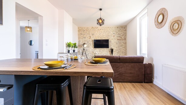 Una cocina moderna con una isla de madera, taburetes negros y una pared de piedra con un televisor.